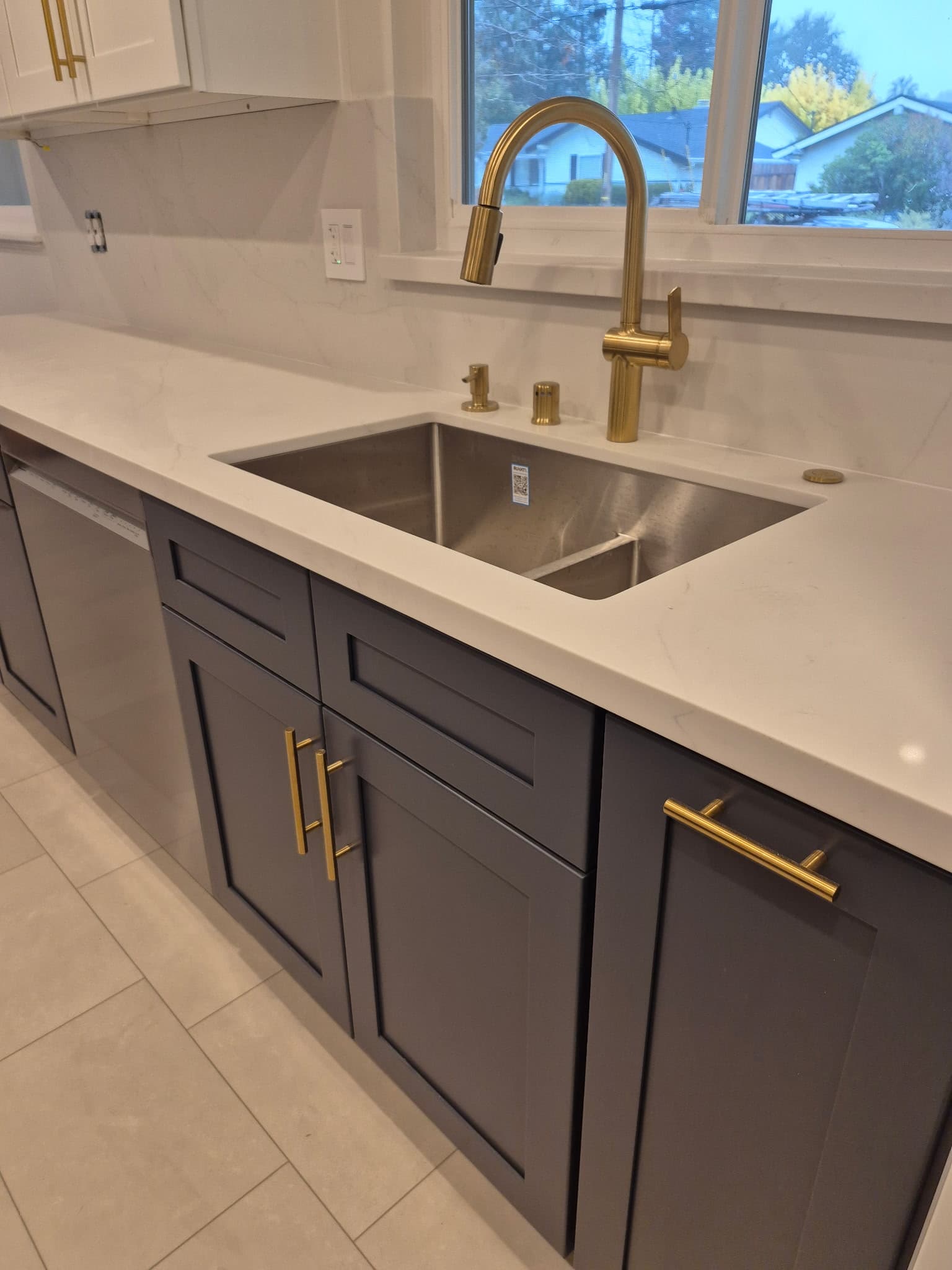 Kitchen detail — quartz countertop, deep undermount sink, and brushed gold faucet against a marble-look backsplash.